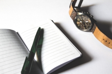 Açık çizgili defter, kalem ve yanındaki kol saati