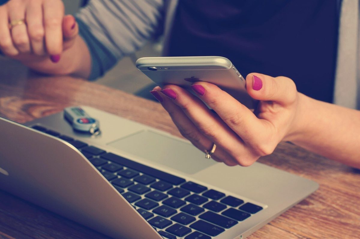 Dizüstü bilgisayarın başında telefonundan işlem yapan kişi
