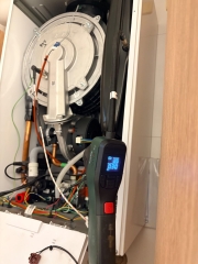 Kapağı açılmış kombide fan, gaz valfi ve kablo tesisatı; önünde dijital basınç göstergesi