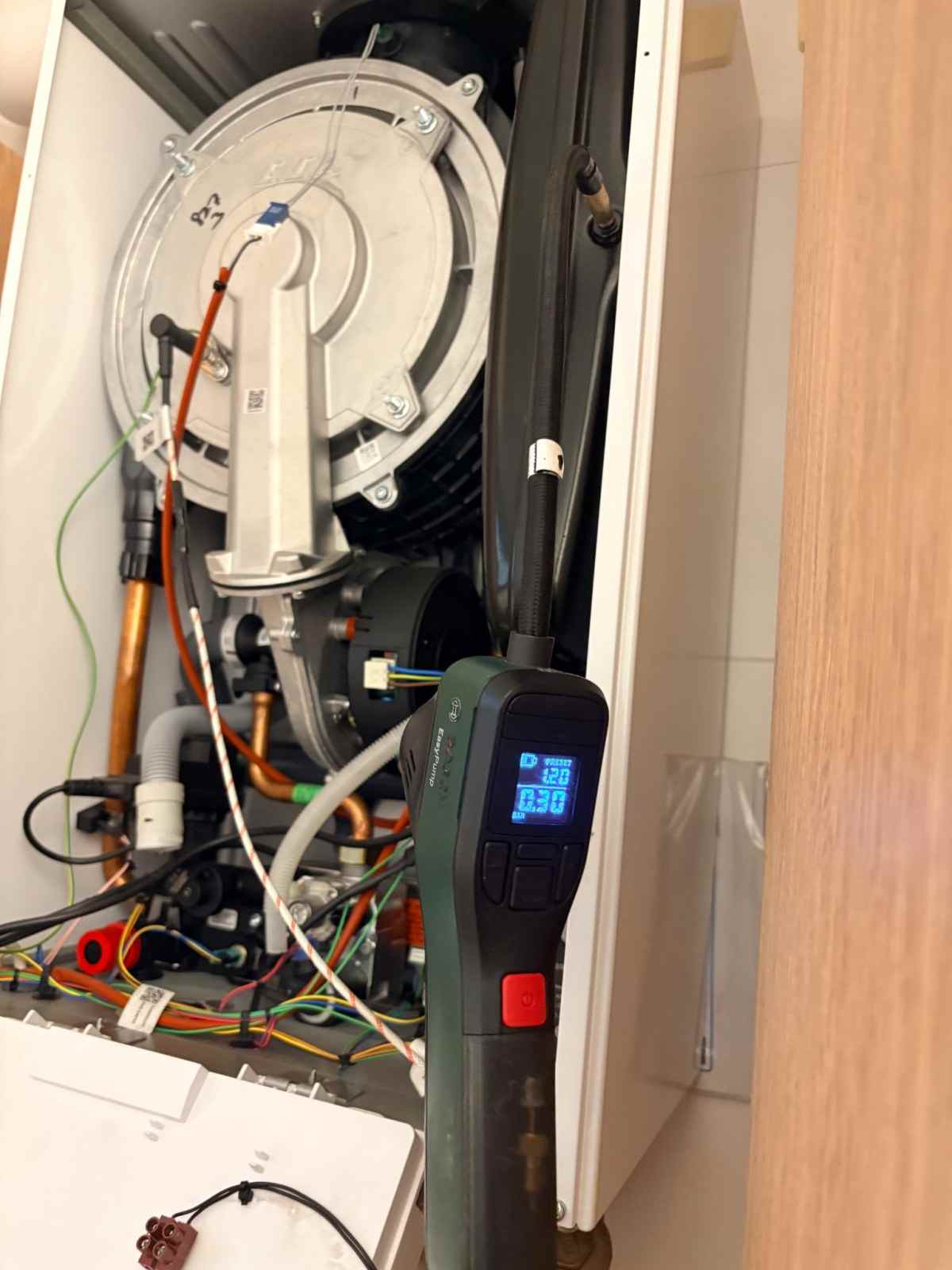 Kapağı açılmış kombide fan, gaz valfi ve kablo tesisatı; önünde dijital basınç göstergesi