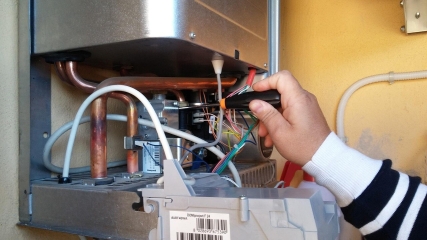 Kapağı açılmış kombide gaz valfi ve bakır boruların üzerinde çalışan teknisyen