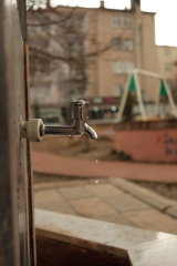 Bahçe musluğundan damlayarak akan su, arkada apartman
