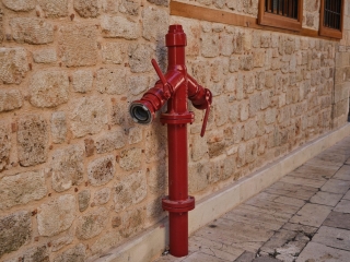 Taş duvarın önünde duran kırmızı yangın hidrantı