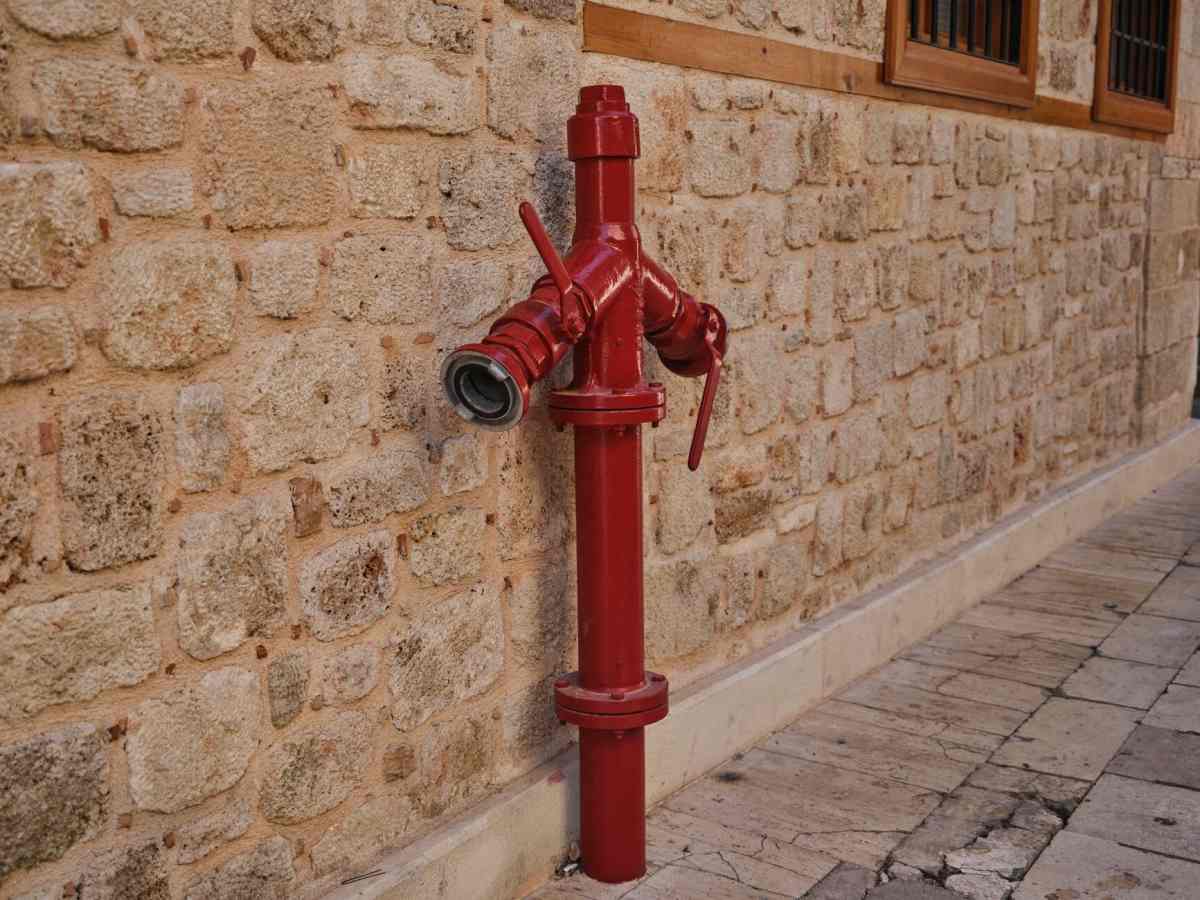 Taş duvarın önünde duran kırmızı yangın hidrantı
